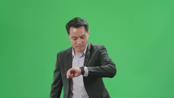 Asian Business Man Walking While Looking At Watch And Run On Green Screen Chroma Key alt