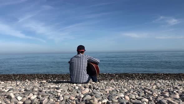 Man Plays on the Guitar at the Sea in Sunny Day