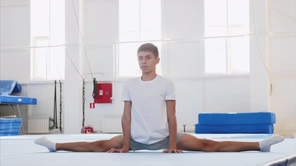 A teenager boy is making a front split in front of the camera.