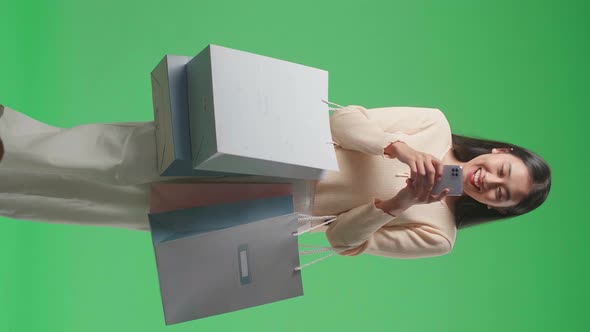 Asian Shopping Woman With Shopping Bags Use Mobile Phone While Walking In Front Of Green Screen alt