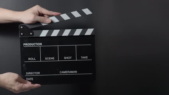 Movie slate or clapperboard hitting. Close up hand holding empty film slate and clapping it on black