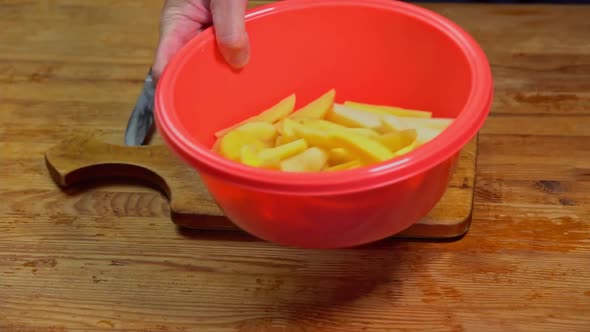 A hand tosses sliced fresh potatoes in a bowl in slow motion. The cook is cutting potato on wooden alt