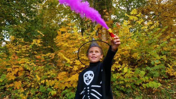 A Boy with Colored Smoke in His Hands in a Skeleton Costume Wearing a Hat During Halloween alt