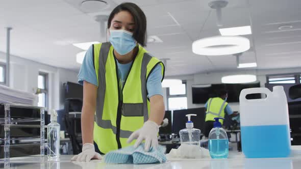 Woman wearing hi vis vest and face mask cleaning the office using disinfectant alt