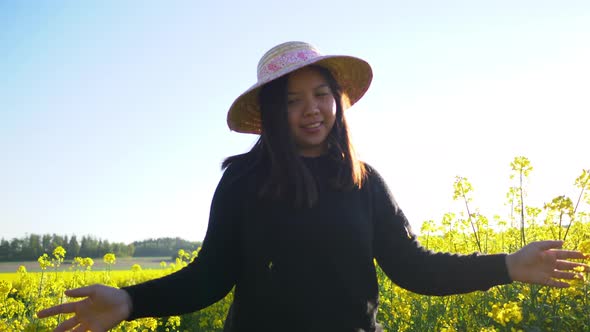 Front view of woman walking and touching flower on track in yellow field alt