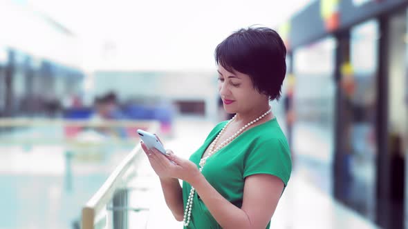 Woman in Green Dress in the Mall Uses the Phone, Reads Information alt