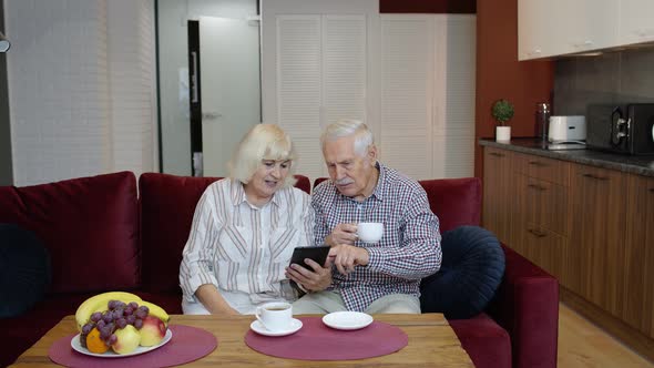 Senior Old Couple Grandparents Talking and Using Digital Tablet Computer at Home. Internet Shopping alt