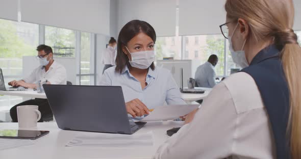 View Over Shoulder of Caucasian Businesswoman Collaborate with African Colleague in Protective Mask alt