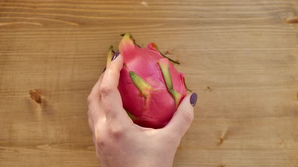 Closeup of Hands Cutting a Pitahaya Fruit with a Black Knife on a Wooden Board