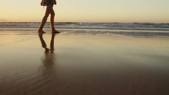 Woman with arms outstretched walking on beach alt