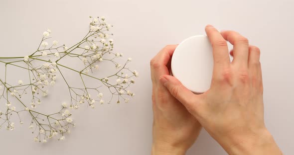 Female hands open jar of green cream or mask with flowers on white background. Luxury green mask 