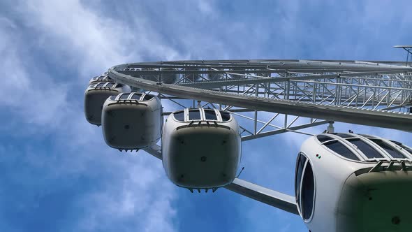 Ferris Wheel with Closed Metal Booths Slowly Rises Against the Blue Sky Bottom View