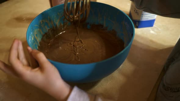 Kid Hand Stirring with a Whisk Melted Dark Chocolate in a Plastic Bowl