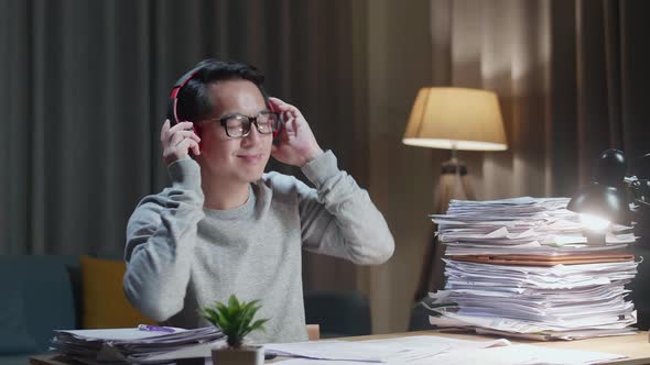 Asian Man Wearing Headphones And Listening To Music After Working With Documents At Home alt