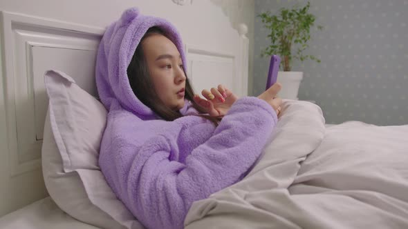 20s Asian Woman Reads Good News on Mobile Phone Lying in Bed