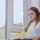 A young woman at home by the window puts on headphones and opens a laptop and gets ready for work. - VideoHive Item for Sale