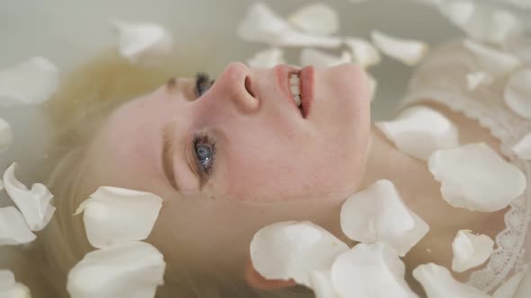 Beautiful Young Blonde Woman Lies in a Bathroom with White Rose Petals