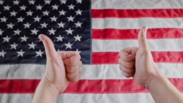 Thumbs Up Gesture Made with Two Caucasian Hands in Front of Blurry US Flag