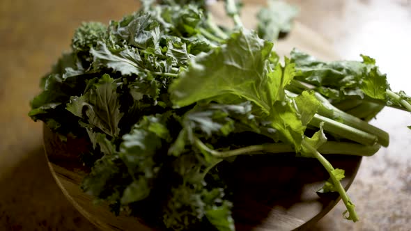Clusters of stalks of fresh rapini on a round cutting board rotating in beautiful backlit light. Sha alt