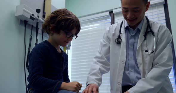 Front view of young asian male doctor examining caucasian boy patient knee in a clinic 4k alt