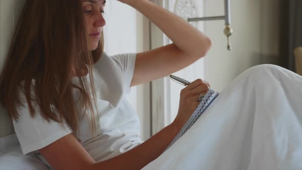 Young Woman Writing Notes to Diary After Awake in Bedroom at Home