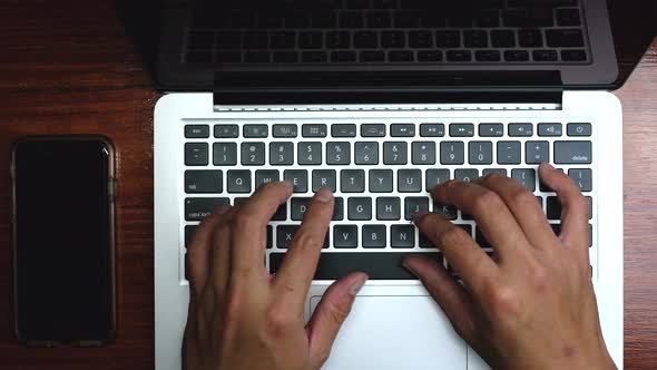 Top view, Male's hand typing on white laptop on wooden desk.