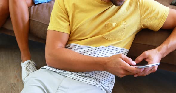 Man text messaging and woman peeking into his mobile phone from behind alt