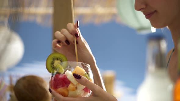 Smiling young woman eating fruit salad at the beach