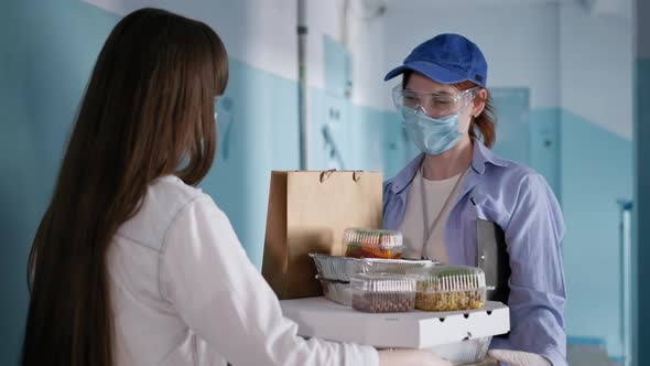 Pandemic, Young Girl in Medical Mask Orders Food By Female Courier Wearing Respirator and Gloves alt
