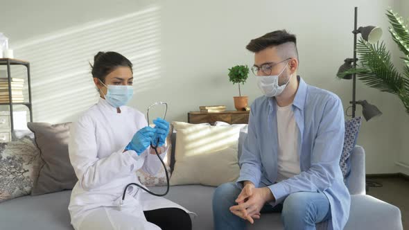 Mixed race female doctor wearing mask and senior man taking blood pressure at home