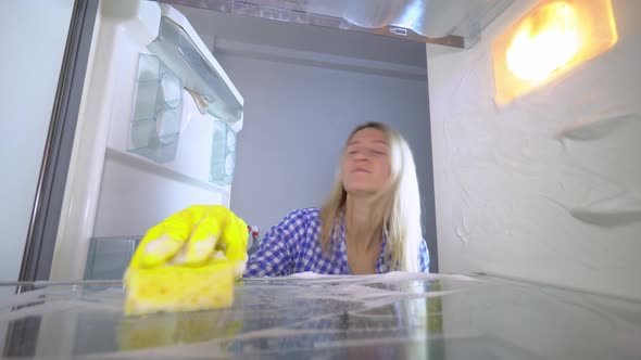 A disgruntled and irritated woman washes and cleans inside the refrigerator alt