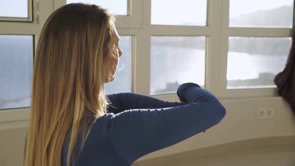 Young Woman Does Sports Exercises for Arms Near Window