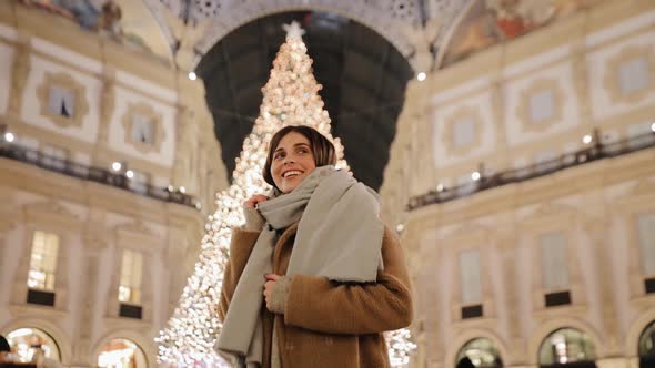 A girl poses against the background of a New Year tree in the evening Milan city alt