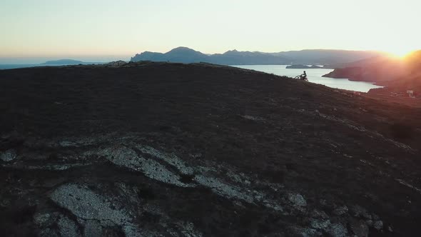 Drone View of Man on Motorbike Extremely Rides Across the Hills with Black Sea on Background in