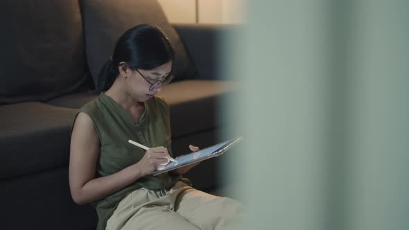 Asian female reading news on her digital tablet while sitting on the sofa in the living room.