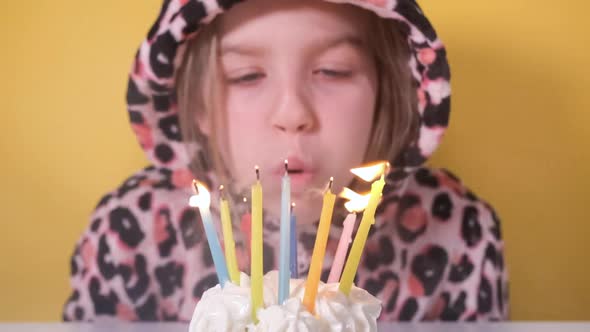 Happy Teen Girl in Leopard Overalls Blows Out Ten Colorful Candles on Birthday Cupcake at Party