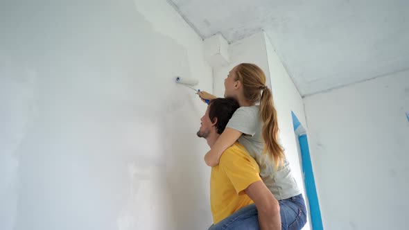 A Happy Man and Woman Paint the Wall Using a Roller Painter alt