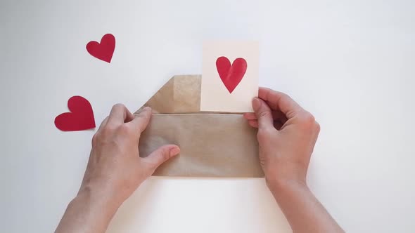 Hands Open an Envelope and Put a Red Heartshaped Valentine There for Valentine's Day