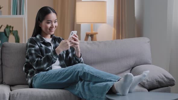 Asian Girl Woman Sitting on Sofa at Home Relaxing Watching News Feed on Social Media Choosing alt