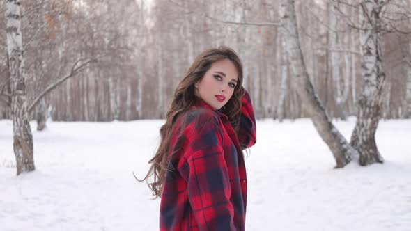 Young Woman with Wavy Hair Standing and Touching Face in Winter Forest