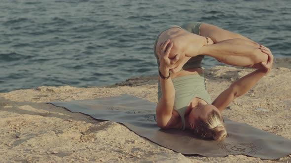 Blond Caucasian Female Yoga Teacher Practicing and Mastering Inverted Lotus Pose on a Cliff in Front