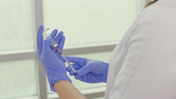 A Doctor in a Medical Mask and Blue Gloves Holds a Syringe and a Vaccine alt