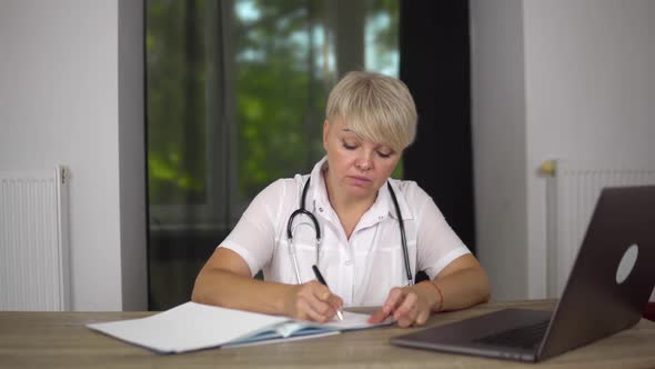 Tired Woman Doctor is Typing the Documents About Illness of Patient to Notebook