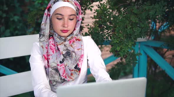 Muslim Woman in Hijab Prints Message on a Laptop, She Is Outside in the Open Air alt