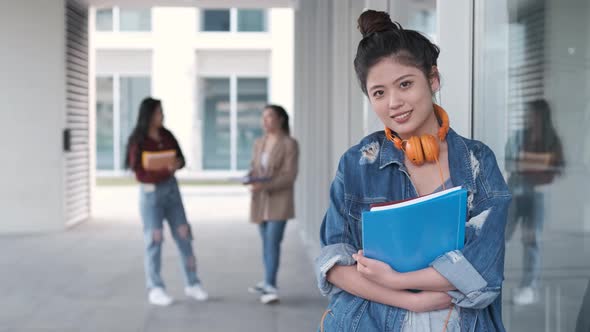 Portrait of an Asian college student holding folders and looking at the camera while standing alt