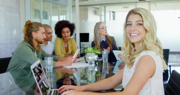 Smiling woman using laptop while colleagues interacting in background 4k alt