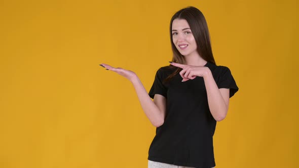 Young Happy girl with long hair in a black T-shirt pointing empty place on her palm