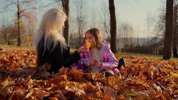 Mother and daughter sitting at autumn forest park. Two females persons spend time together outdoors alt