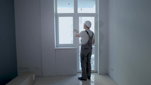 A Builder in Uniform Checks the Size and Quality of Window Installation in a New Apartment alt