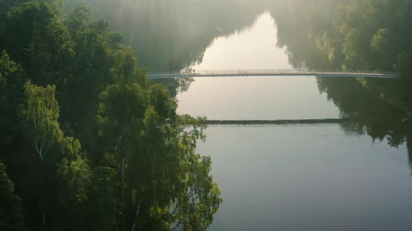 Backpacker walks across bridge over river on sunny day, drone shot alt